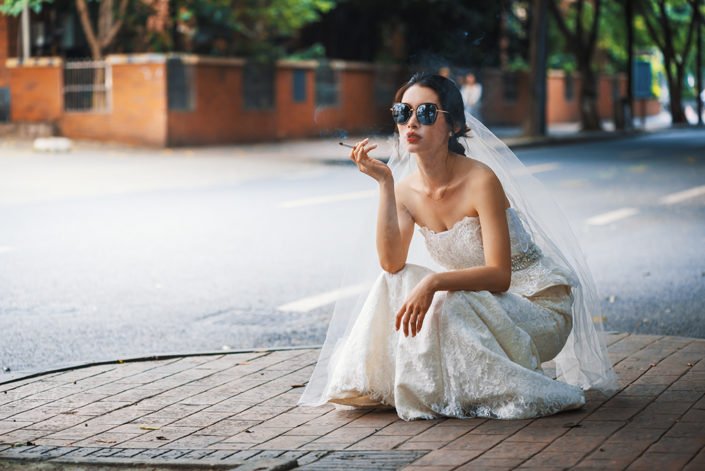 Young chinese bride with sunglasses squat in the street and smoking a cigarette in Chengdu, Sichuan province, China