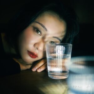 Young woman looking through a glass of water, Chengdu, Sichuan province, China