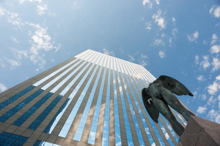 Low angle view of an angel statue and a building against the blue sky in the business district of La Defense, Paris - France. The statue is from Igor Mitoraj and is called "Ikaria"