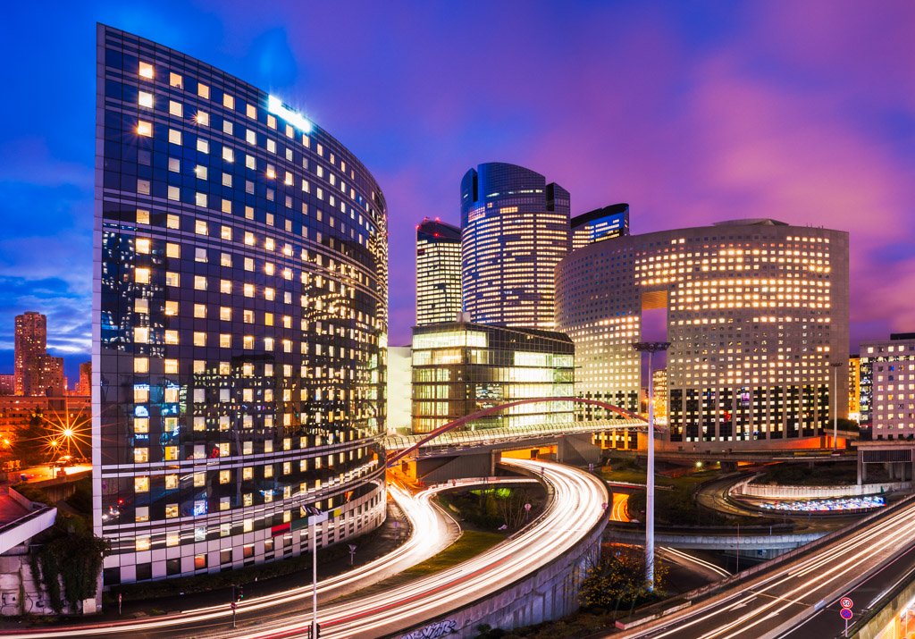 La Defense business district at night with lights in the buildings and car light trails on the roads, Paris, France