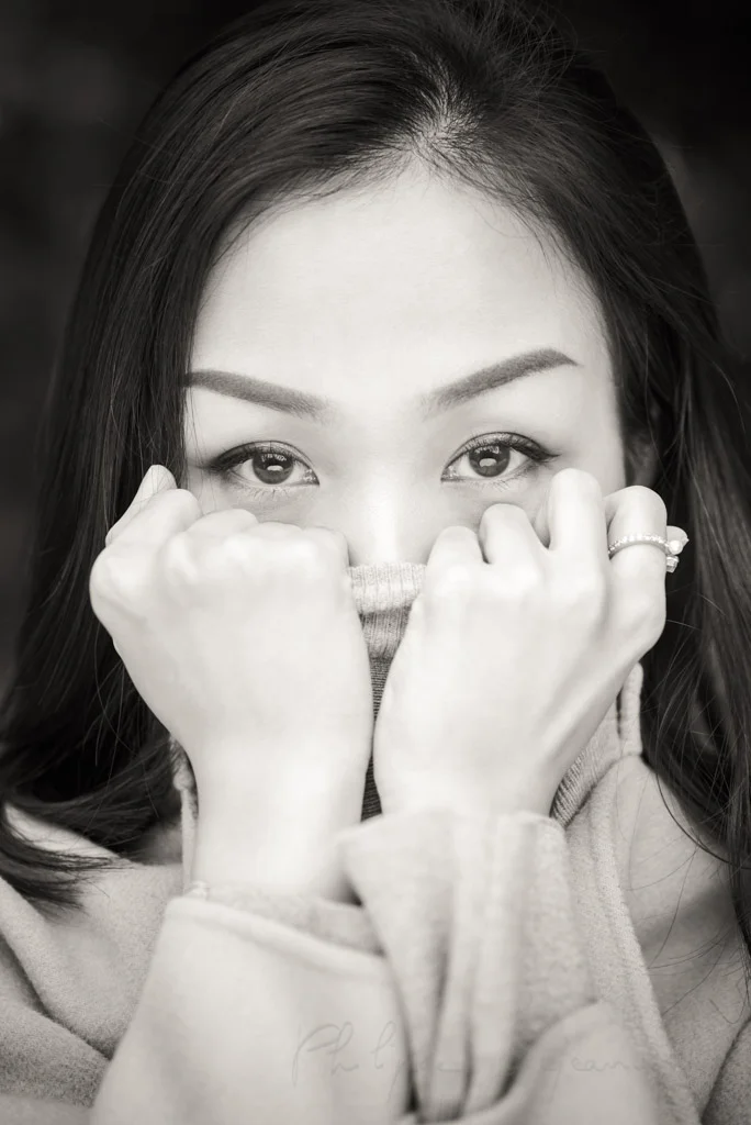 Young chinese woman with long black hair looking at the carmera wearing a turtleneck sweater and holding it with her hands in front of her mouth black and white close-up portrait. in Chengdu, Sichuan province, China - Model : Fanny