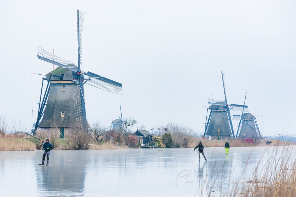 Ice skaters and Windmills in winter with frozen water in a canal in Kinderdijk, Netherlands