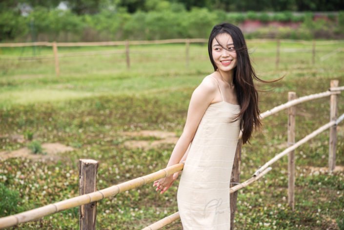 Chinese young woman portrait in nature near a fence in a field, in Chengdu, Sichuan province, China