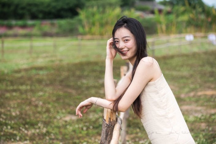Chinese young woman portrait in nature near a fence in a field in Chengdu, Sichuan province, China