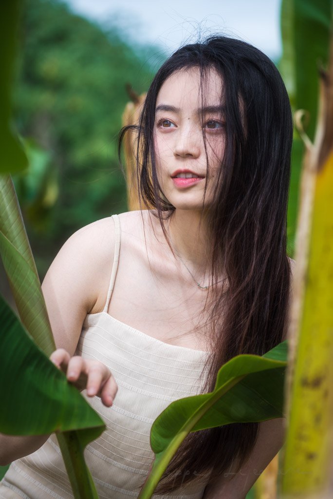 Chinese young woman portrait behind a leaf in nature, Chengdu, Sichuan province, China