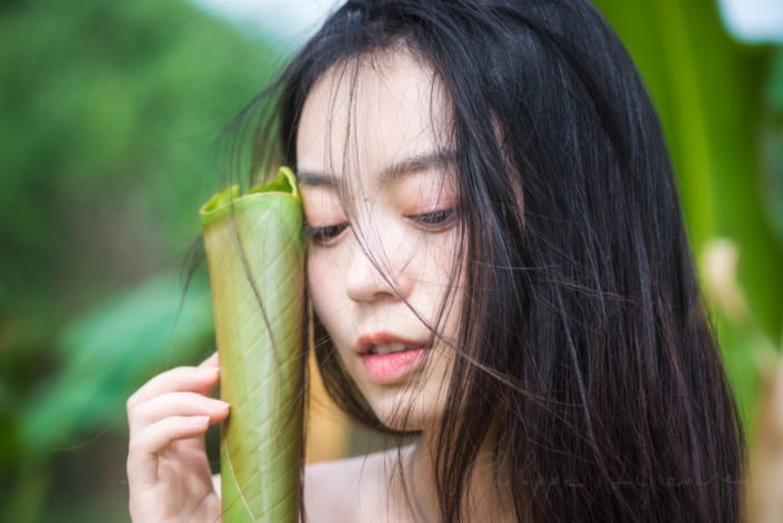 Chinese young woman portrait behind a leaf in nature, Chengdu, Sichuan province, China