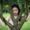 Chinese young woman holding a tree in nature, Chengdu, Sichuan province, China