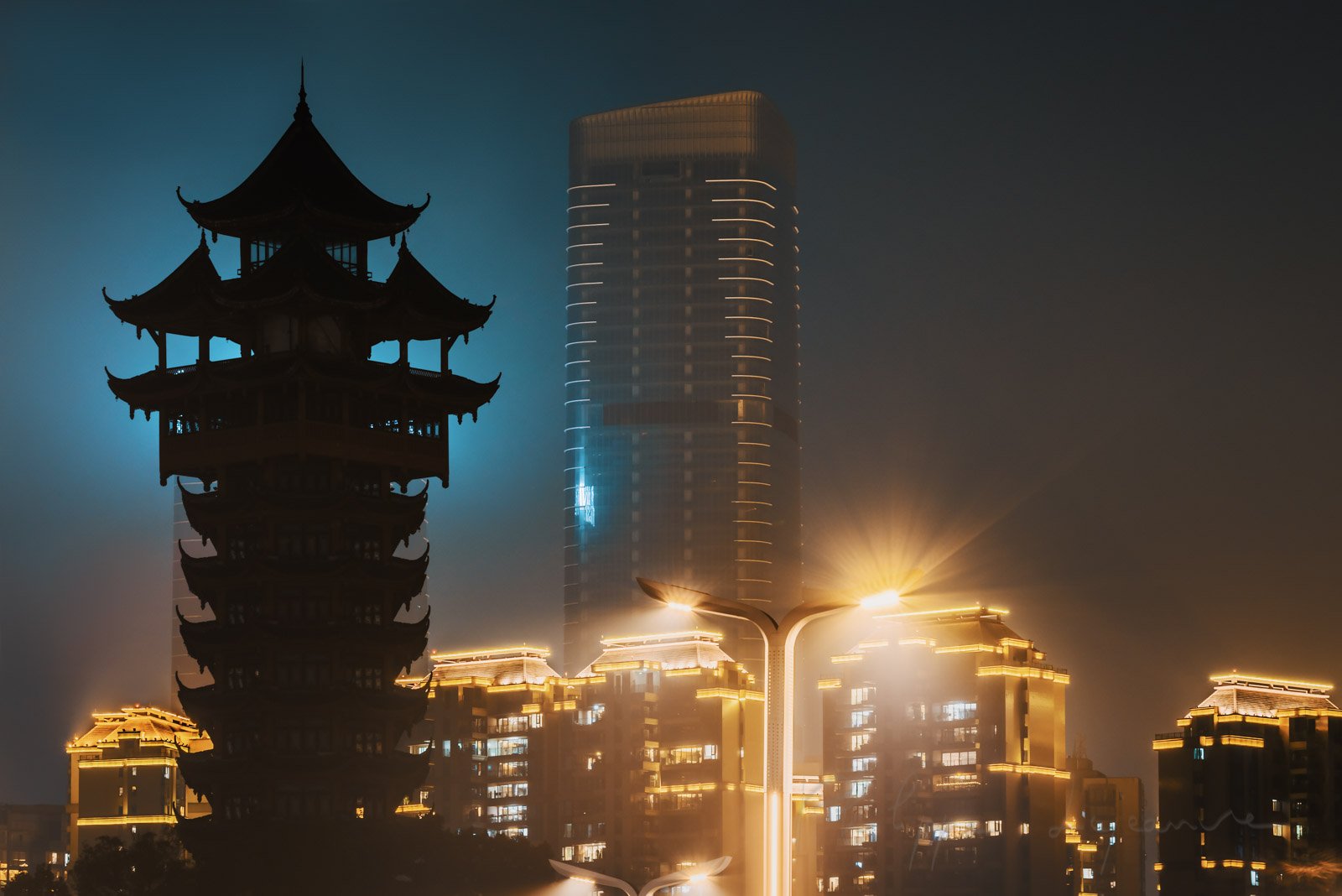 Jiutian tower silhouette in the fog at night against illuminated buldings and skyscrapers in Chengdu, Sichuan province, China