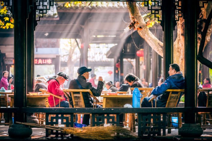 Chengdu, China : People sitting on bamboo chairs and having tea in People's park famous HeMing teahouse with sunrays in the background.