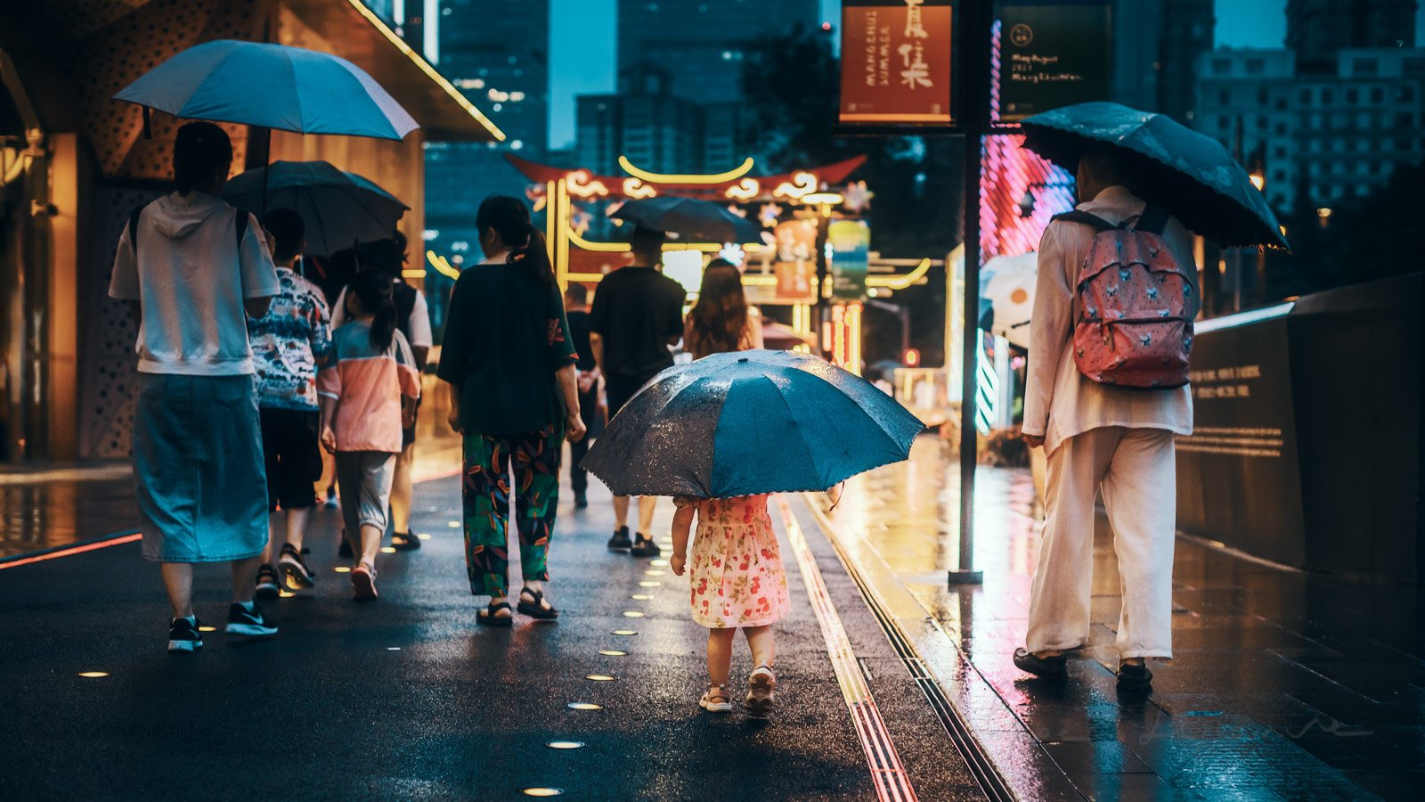 Little girl with a big umbrella wlaking with people under the rain at night in the city, Chengdu, Sichuan province, China