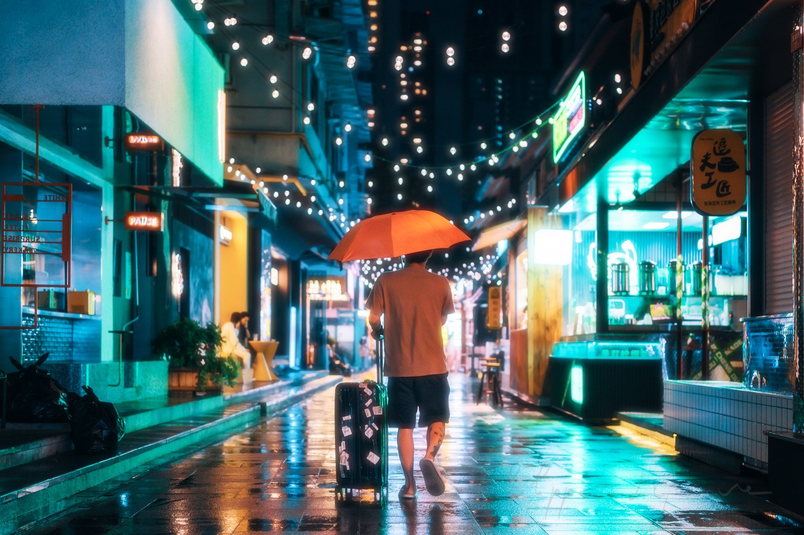 Young traveller with luggage in an illuminated street at nighty under the rain, Chengdu, Sichuan province, China