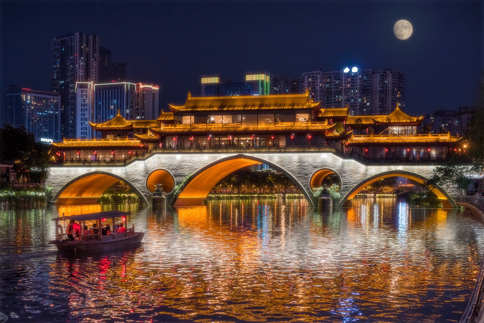 Anshun bridge illuminated at night with full moon. A chinese ancient little boat with red chinese lanterns is sailing on the Jinjiang river for the mid-autumn moon festival