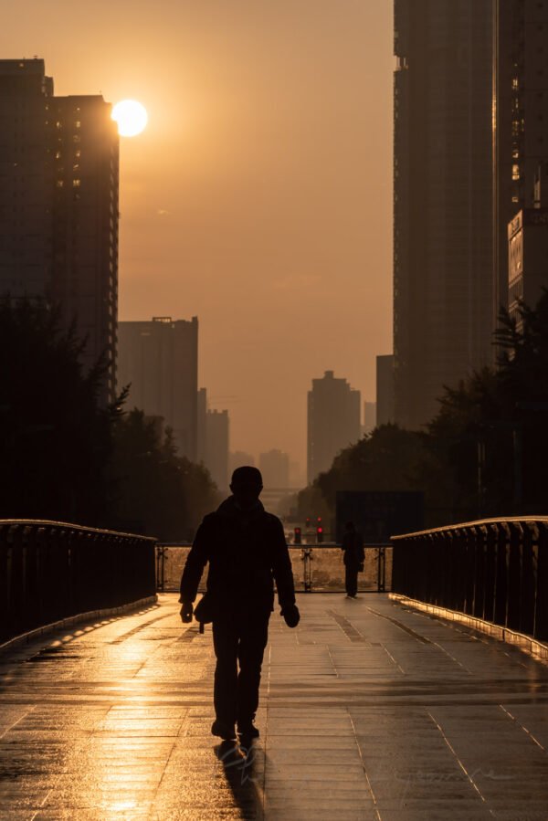 Man walking on a foot bridge against sunrise in downtown Chengdu city, Sichuan province, China