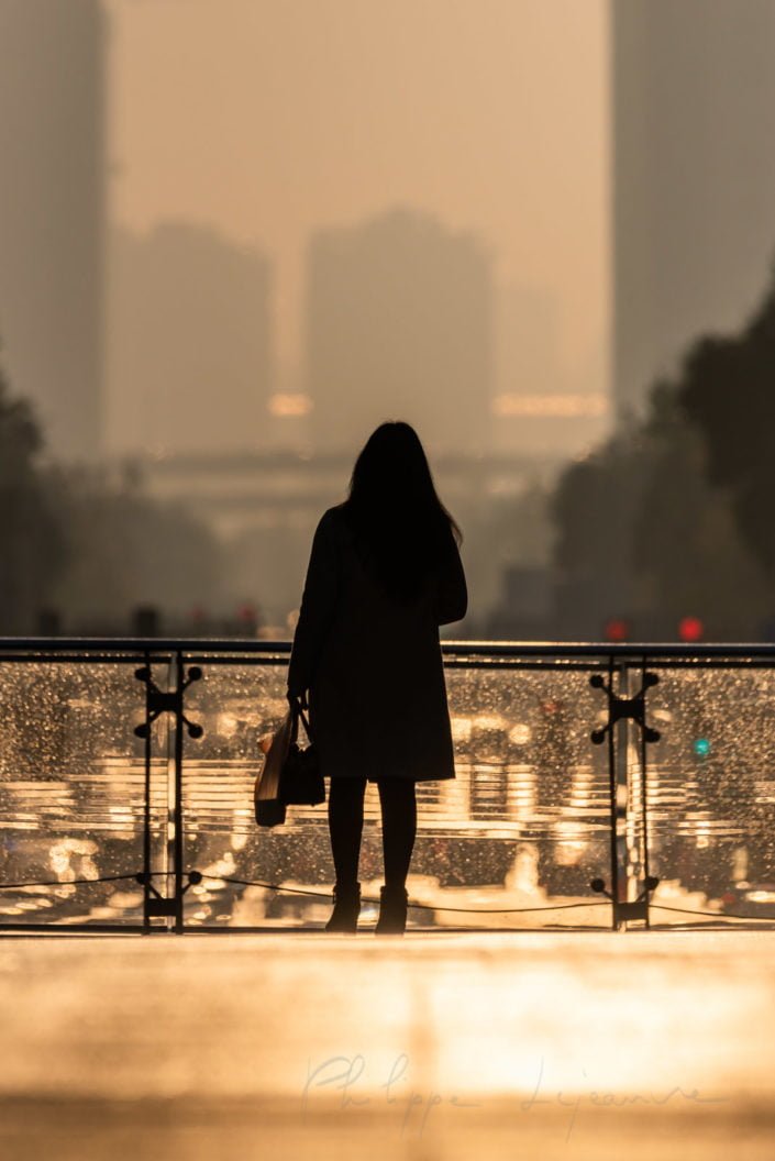 Woman standing on a foot bridge at sunrise in downtown Chengdu city with car traffic in the background, Sichuan province, China