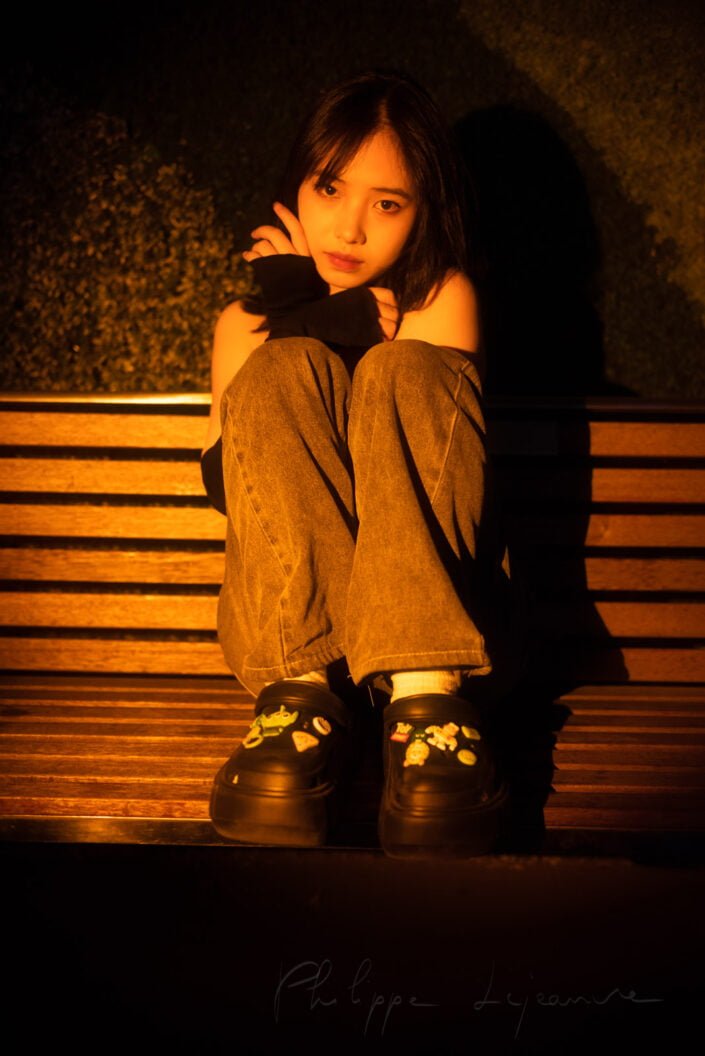 Young Chinese woman sitting on a bench in the street portrait in a spotlight at night in Chengdu