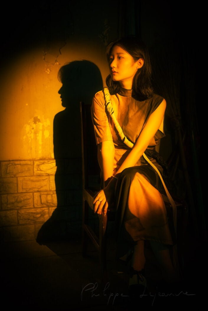 Young Chinese woman sitting on a chair in the street in a spotlight vintage portrait at night in Chengdu