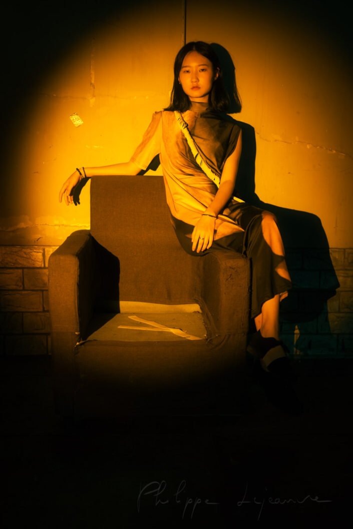 Young Chinese woman sitting on an armchair in the street in a spotlight vintage portrait at night in Chengdu