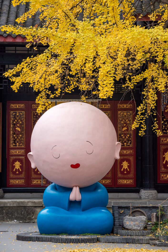 Manga monk statue under a ginkgo tree with yellow leaves in autumn in DaCi buddhist temple, Chengdu, Sichuan province, China