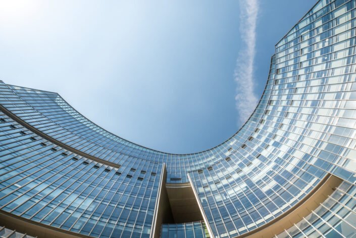 Modern curved glass buildings facade against blue sky directly below view
