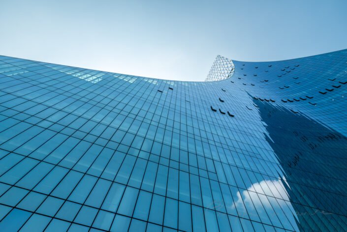 Modern curved glass building facade reflecting clear blue sky