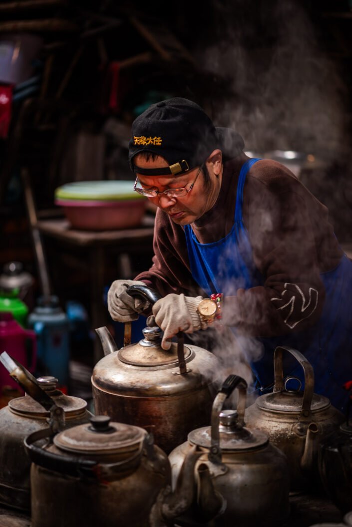 Man arranging ancient teapots on a charcoal oven in PengZhen teahouse, Shangliu, Sichuan province, Chengdu