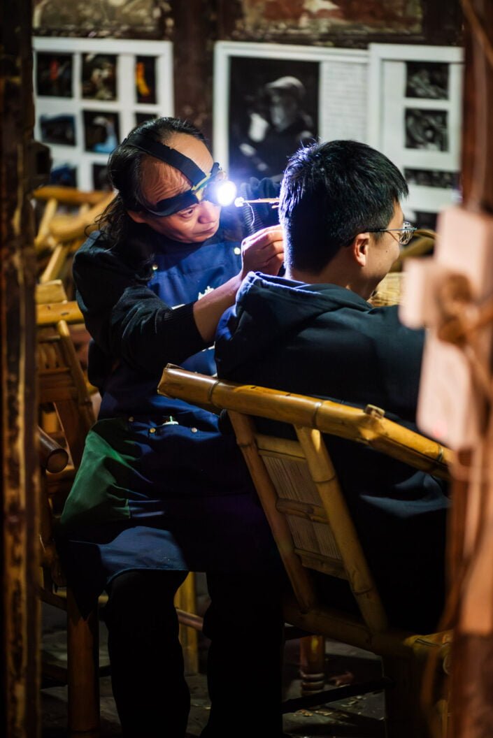 Man cleaning ears of a client in an ancient teahouse in PengZhen teahouse, Shuanliu, Chengdu, China