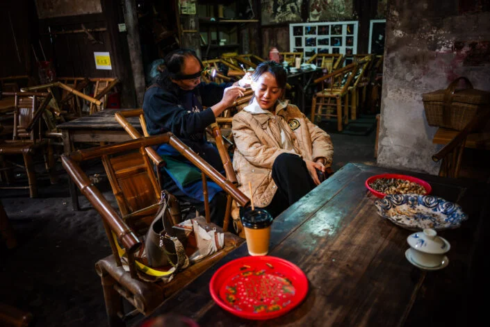 Man cleaning ears of a client in an ancient teahouse in PengZhen teahouse, Shuanliu, Chengdu, China