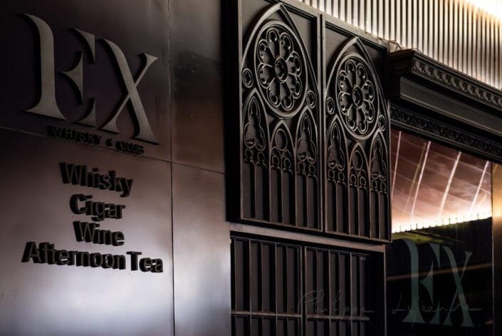 Sophisticated signboard for a club located in Chengdu, at the southern region of the Sichuan province in China. The sign reads 'EXP Whiskey Club,' with 'Whisky Cigar Wine Afternoon Tea' inscribed beneath. The sign is constructed from dark wooden material with large, decorative windows and a modern, sleek alphabet font. This image evokes a sense of luxury and leisure, suggesting a high-end venue for patrons to indulge in fine spirits and tobacco. The overall mood is one of exclusivity and relaxation, inviting viewers to imagine themselves partaking in such an opulent experience.