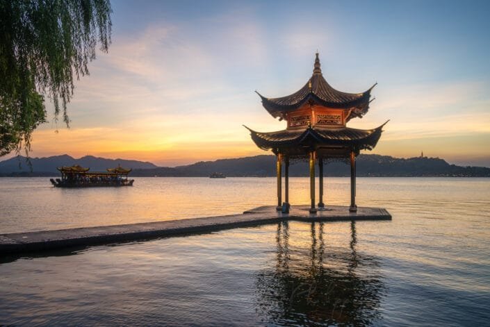 A tranquil moment at sunset as the soft, warm hues illuminate the stunning Jixian pagoda on calm waters. Hangzhou, Zhejiang province, China